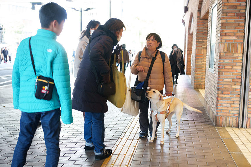 道が分からなくなったら、通行人に聞きます。これもアイメイト歩行の一部。皆さんも街で困っている視覚障害者を見かけたら、勇気を出して「何かお困りですか」と声をかけてみましょう